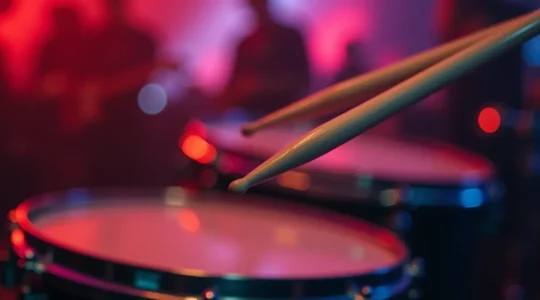 Gros plan sur une paire de baguettes de batterie tenues avec énergie au-dessus d'une batterie acoustique, ambiance rock dynamique